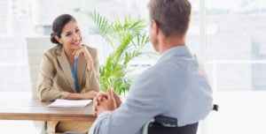 woman in brown blazer speaking with man in wheelchair